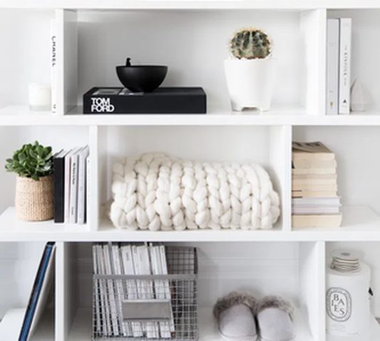 Opgeruimde witte kast met boeken, plantjes en een gebreid kleed